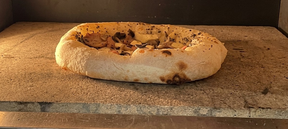 Upieczona pizza w piekarniku z mocno wyrośniętymi i zarumienionymi brzegami.