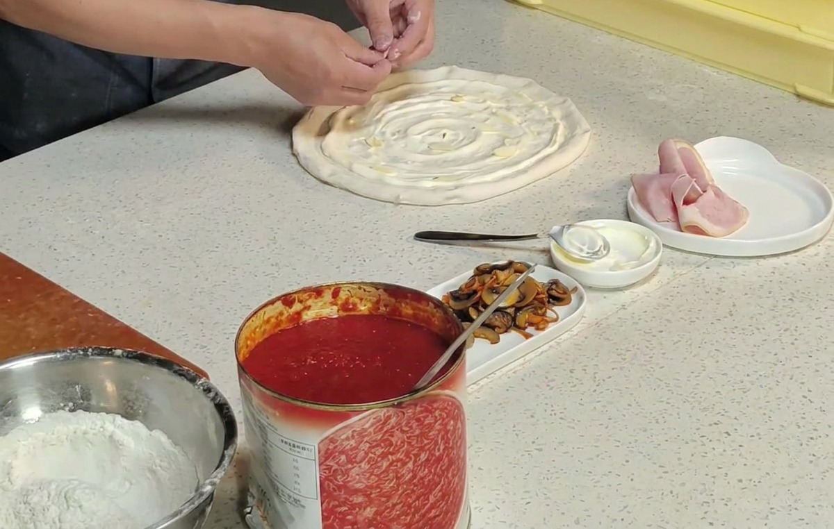 Dłonie kucharza układające pomarańczowe kwiaty maczużnika na surowym spodzie pizzy.