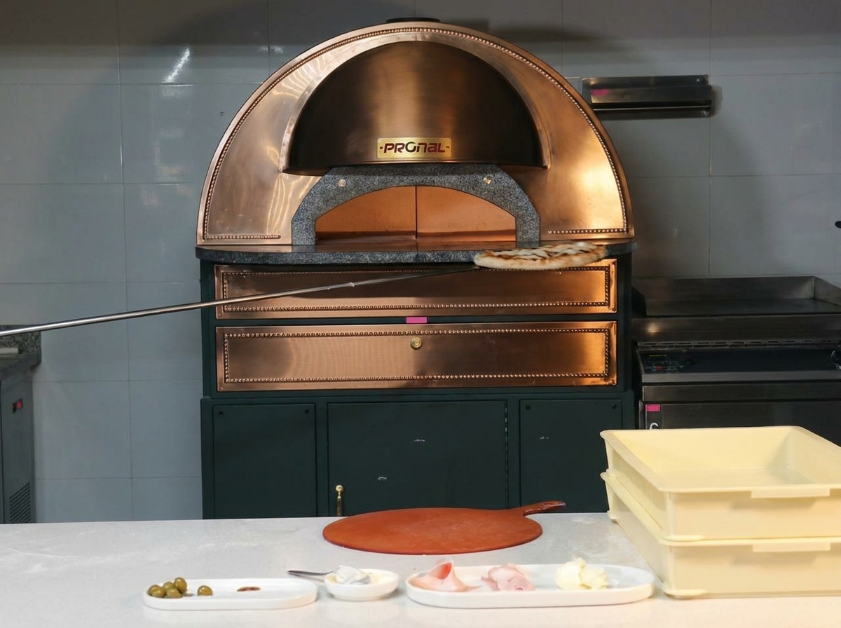 Upieczona pizza z przypieczonymi brzegami wyjmowana z miedzianego pieca na metalowej łopacie.