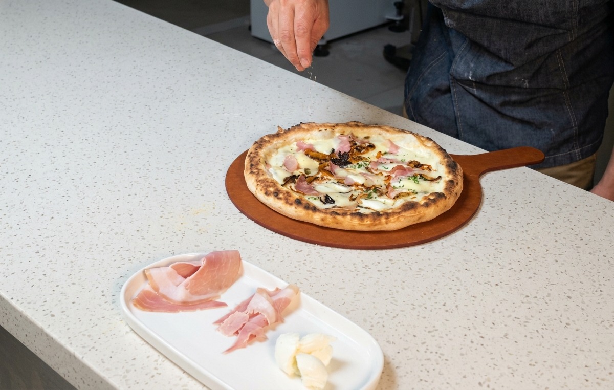 Dłoń kucharza posypująca gorącą, świeżo upieczoną pizzę tartym serem.