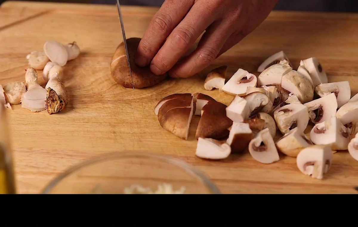 Dłonie krojące świeże shiitake i pieczarki na drewnianej desce.