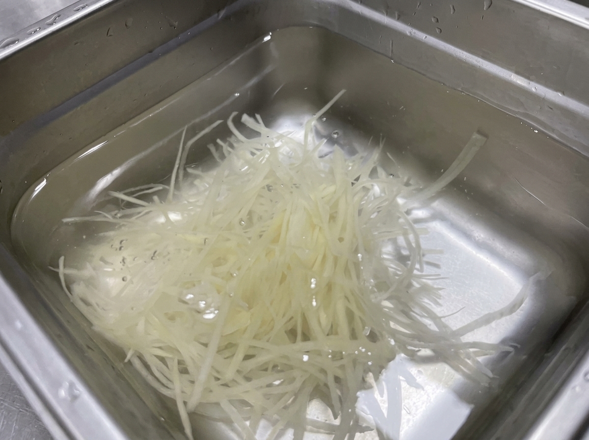Słupki ziemniaków julienne zanurzone w stalowej misce z czystą wodą.