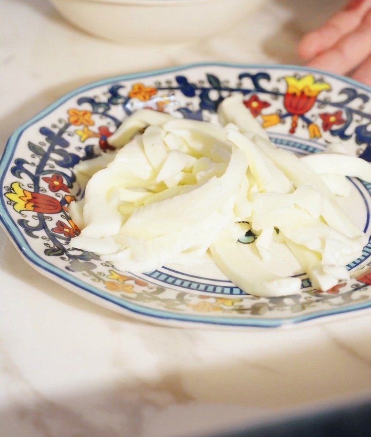 Równomierne paski białego sera fior di latte na małym talerzyku.