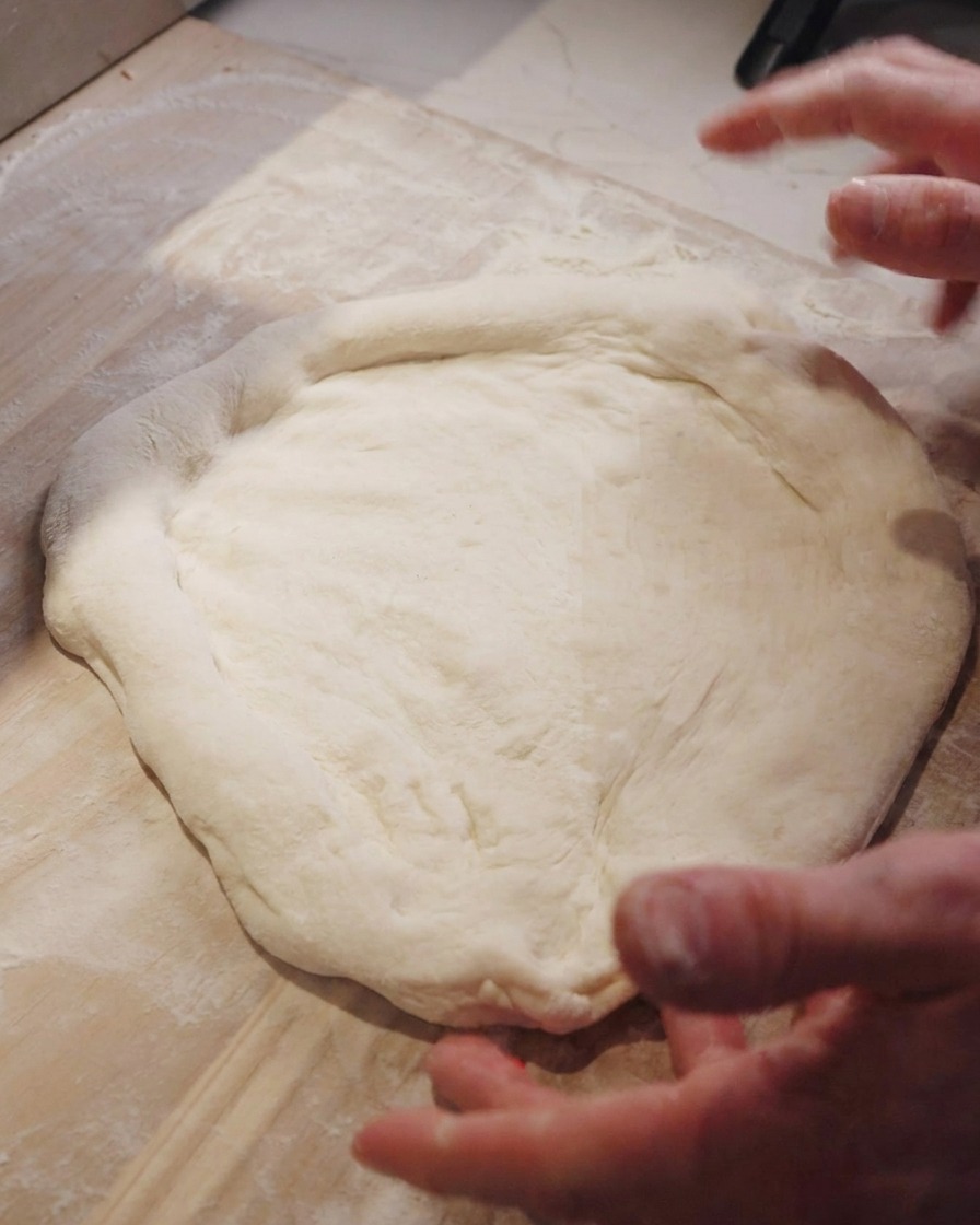 Dłonie szefa kuchni rozciągające spód do pizzy na drewnianym blacie.