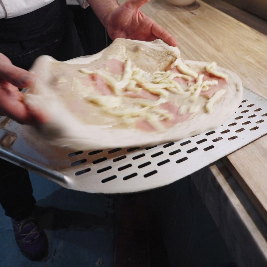 Surowa pizza na metalowej łopacie z kremem truflowym, szynką i słupkami sera.