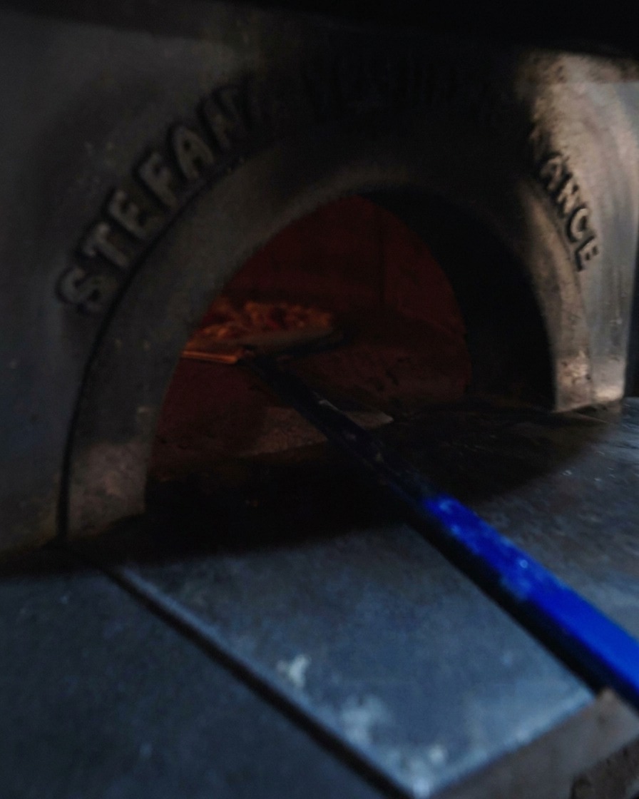 Niebieska łopata wsuwająca przygotowaną pizzę do rozgrzanego pieca opalanego drewnem.
