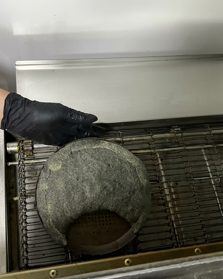 Surowe czarne calzone na metalowej blasze wjeżdżające do pieca taśmowego.