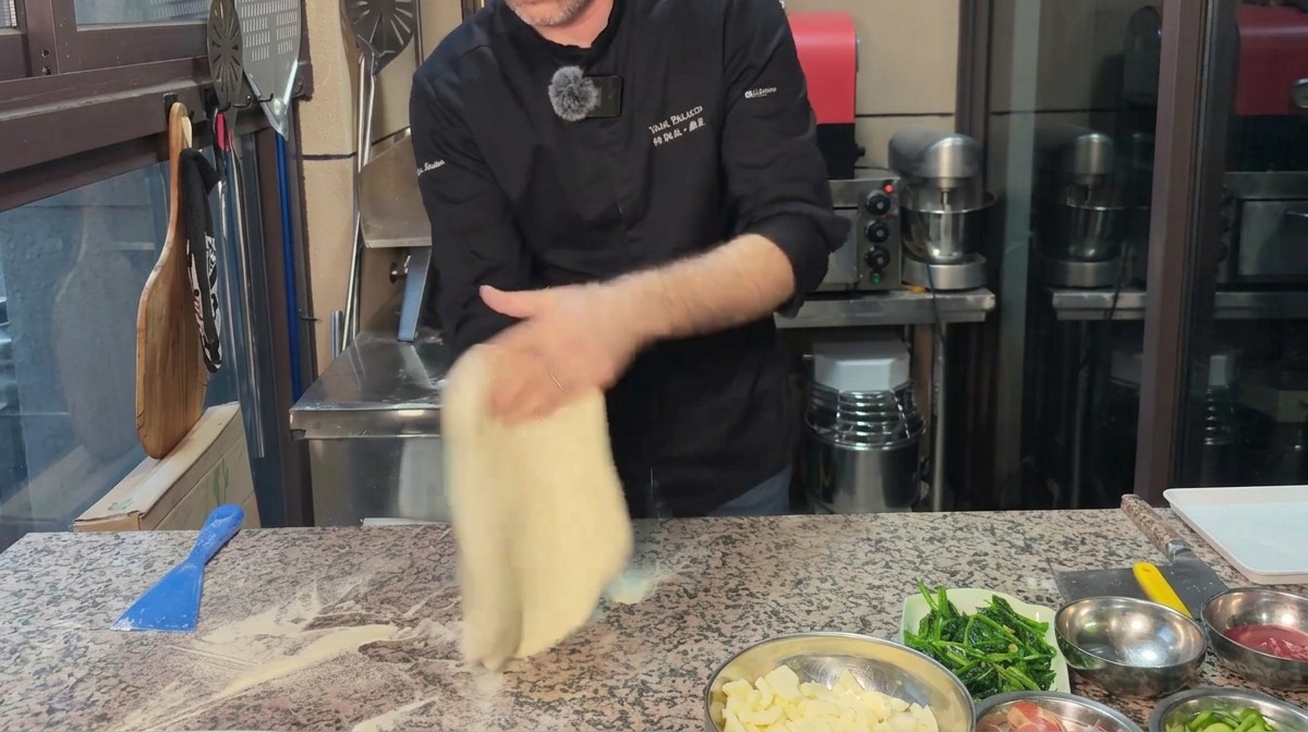 Szef kuchni rozciągający ciasto na pizzę w koło na oprószonym mąką blacie.