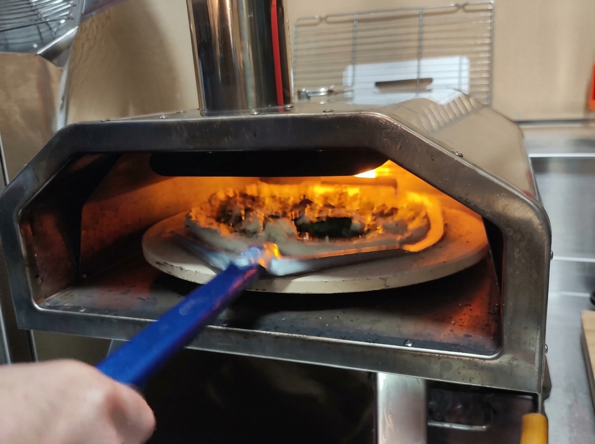Użycie perforowanej łopaty do włożenia surowej pizzy do gorącego pieca.