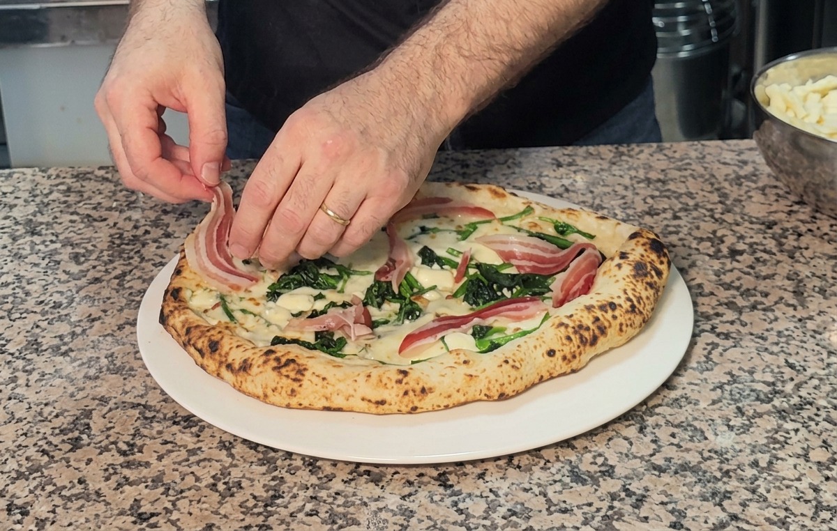 Układanie cienkich plastrów boczku pancetta na świeżo upieczonej, gorącej pizzy.