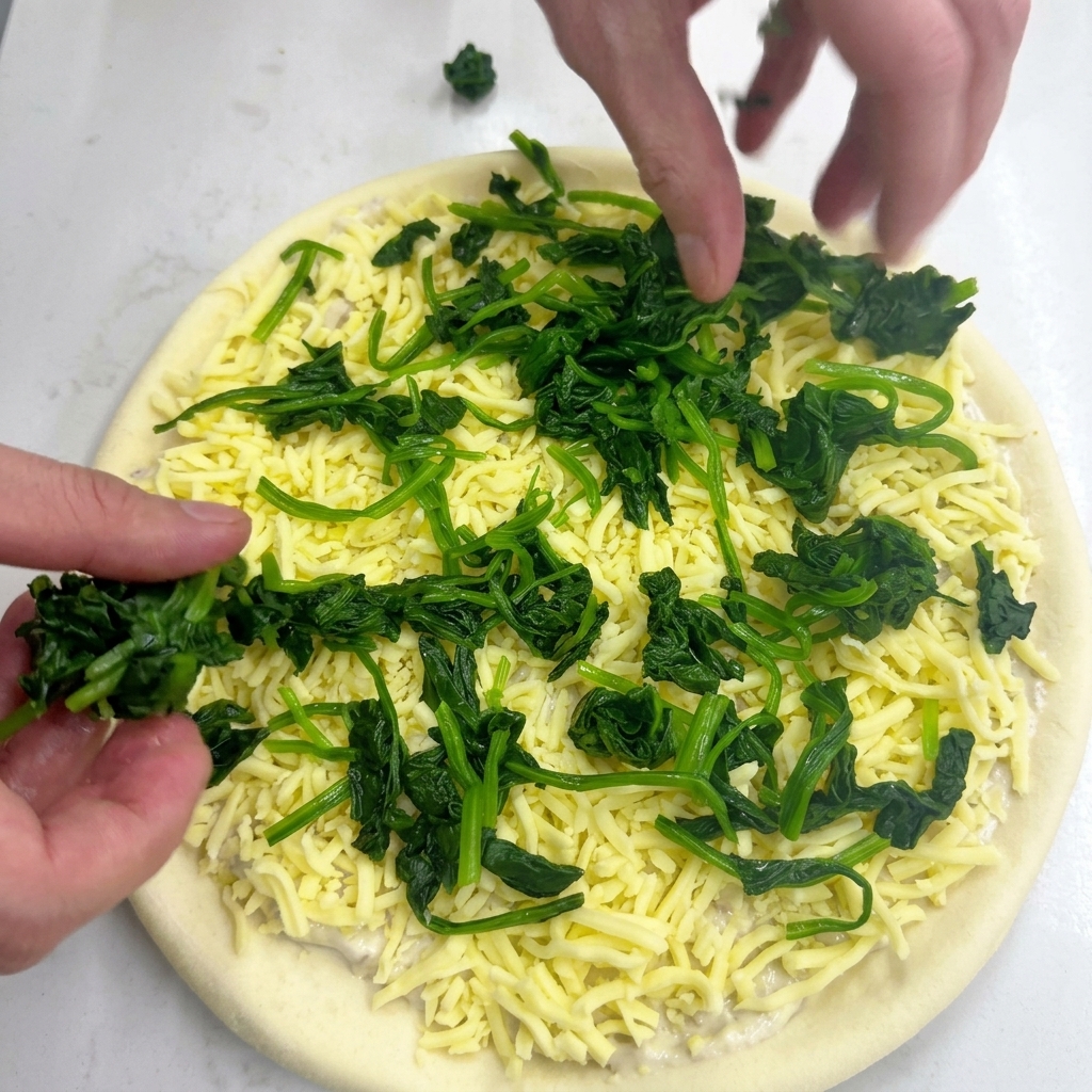 Dłonie układające kępki zblanszowanego zielonego szpinaku na serze mozzarella.