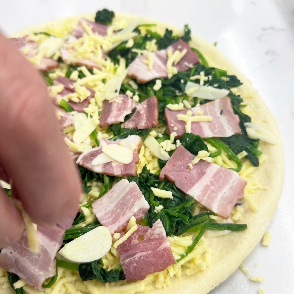 Ręka posypująca surową pizzę dodatkową porcją mozzarelli na wierzchu składników.