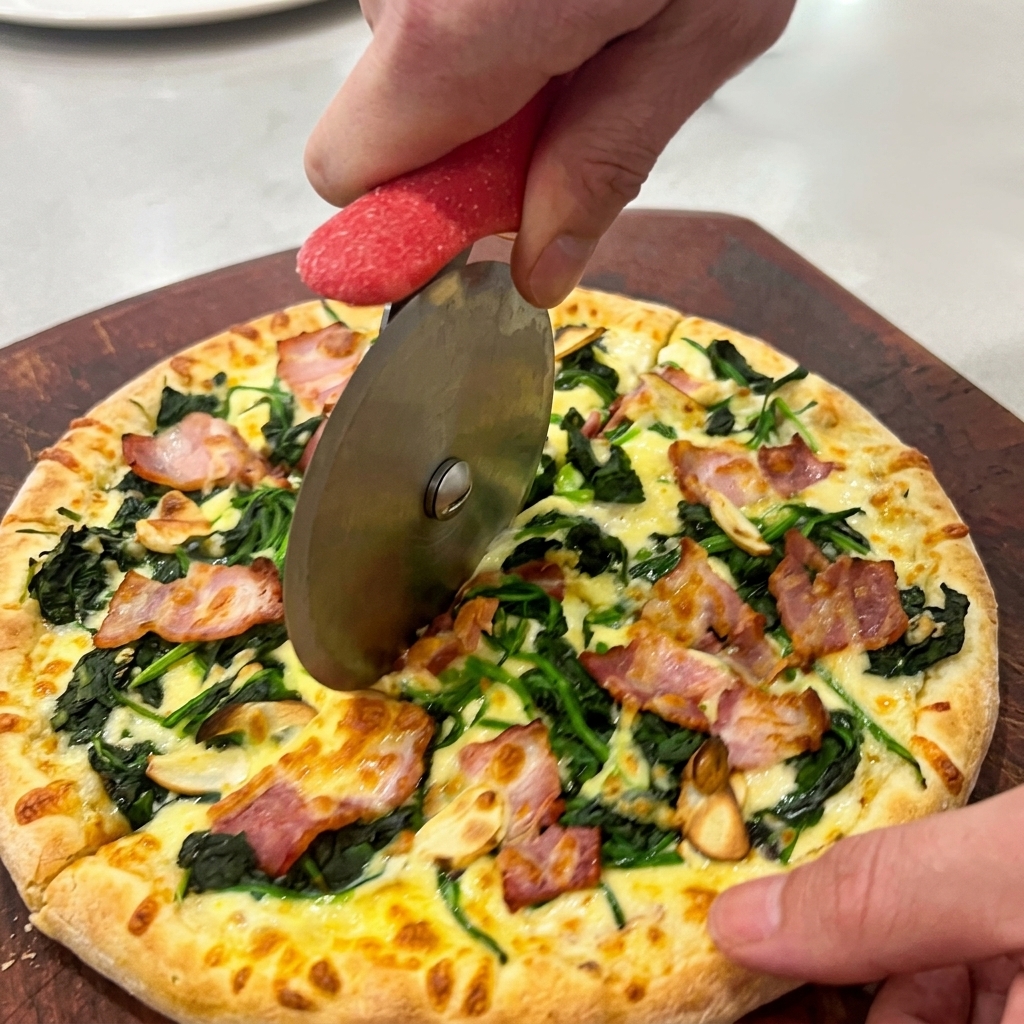 Ręce krojące gorącą pizzę radełkiem na ciemnej drewnianej desce.