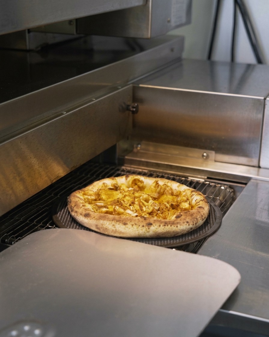 Pizza z owocami morza w piecu; brzegi ciasta wyrastają i nabierają brązowego koloru.