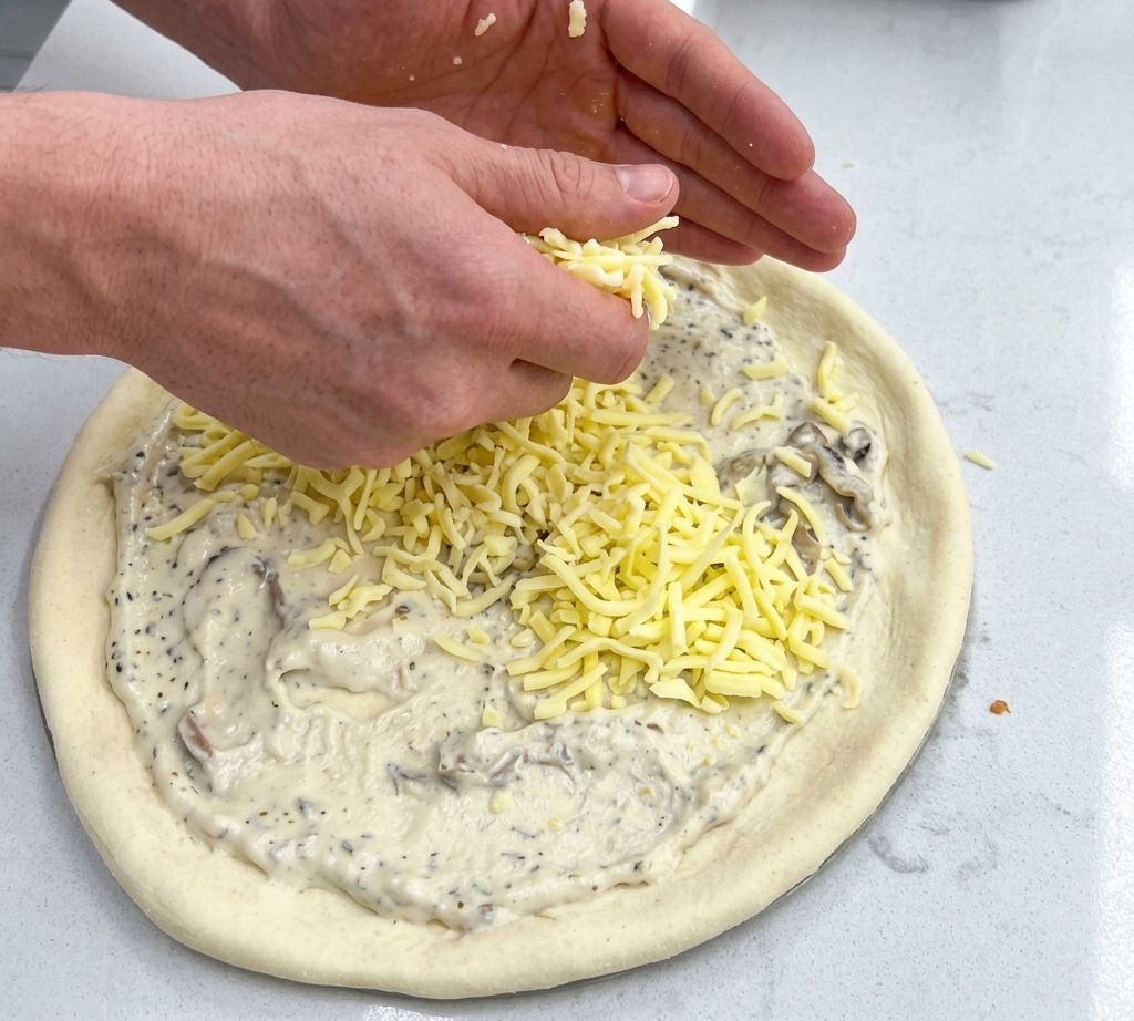Posypywanie spodu pizzy z sosem obfitą warstwą tartego sera mozzarella.