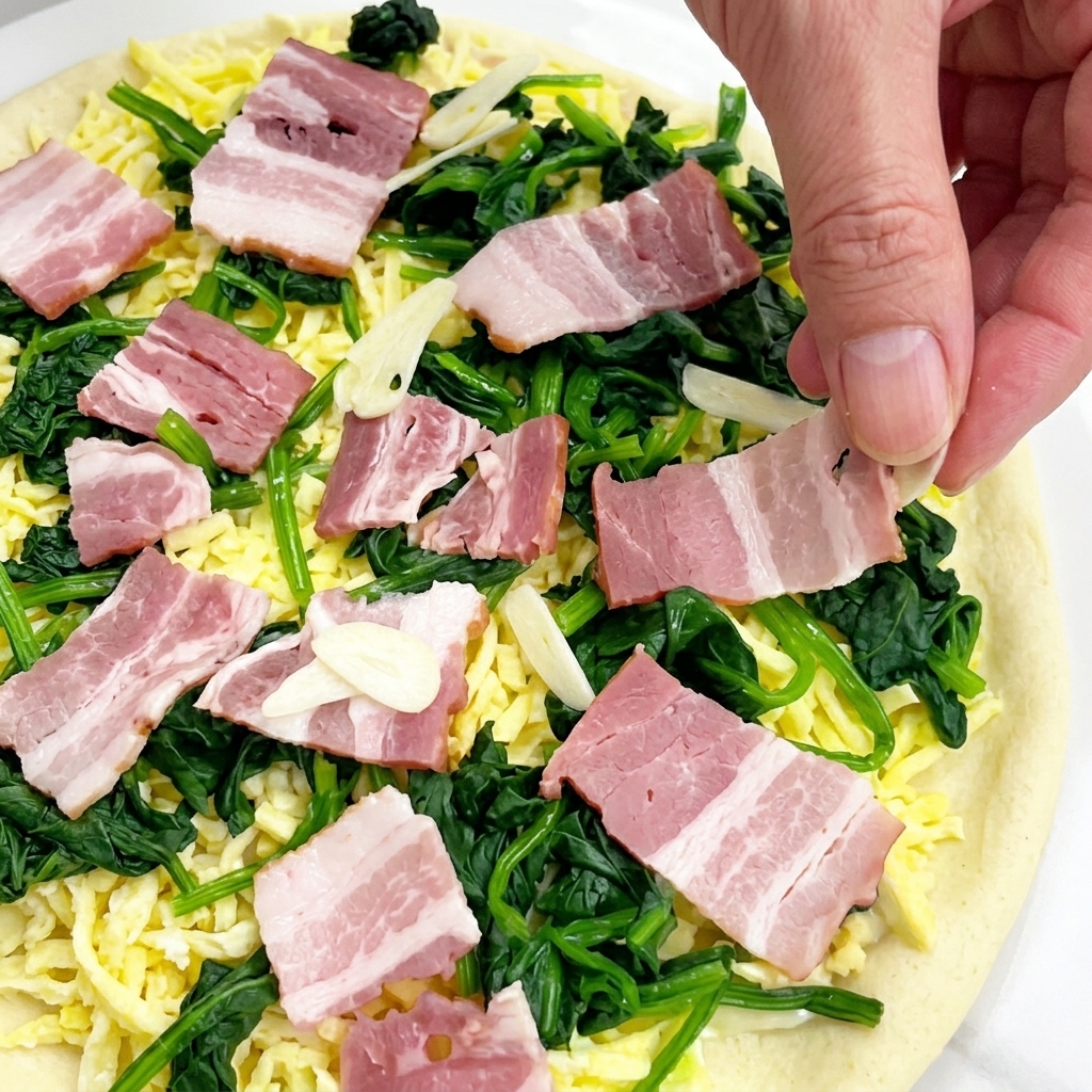 Posypywanie pizzy cienkimi plasterkami surowego czosnku.