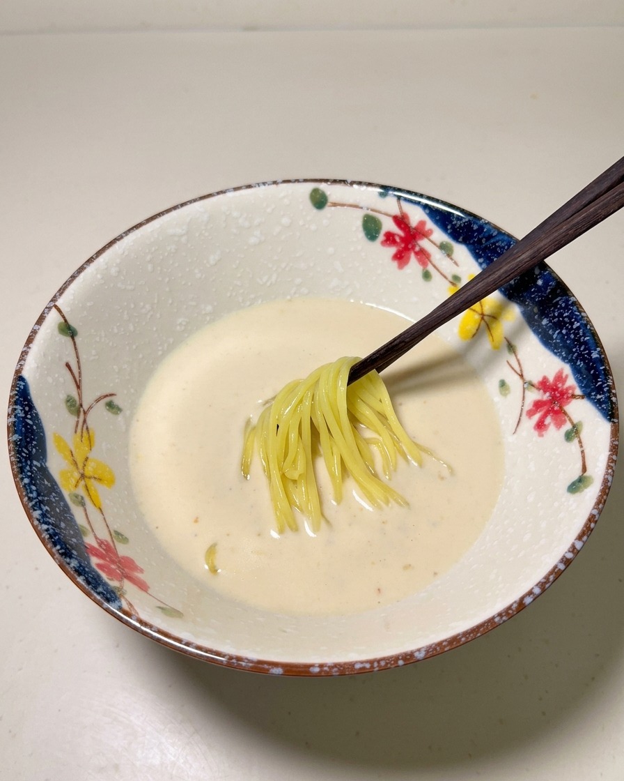 Ugotowany żółty makaron ramen wkładany do kremowej bazy w dekoracyjnej misce.