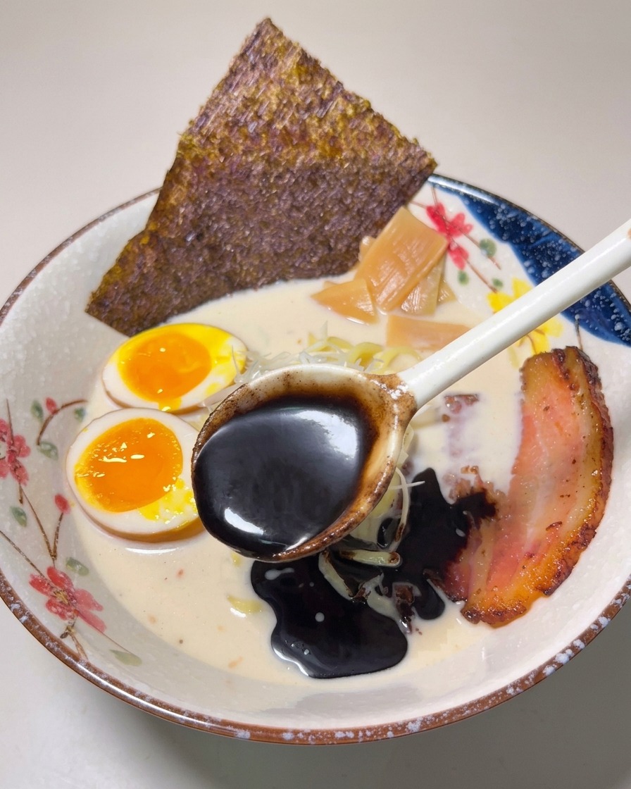 Łyżka gęstego, czarnego oleju czosnkowego polewająca gotowy ramen.