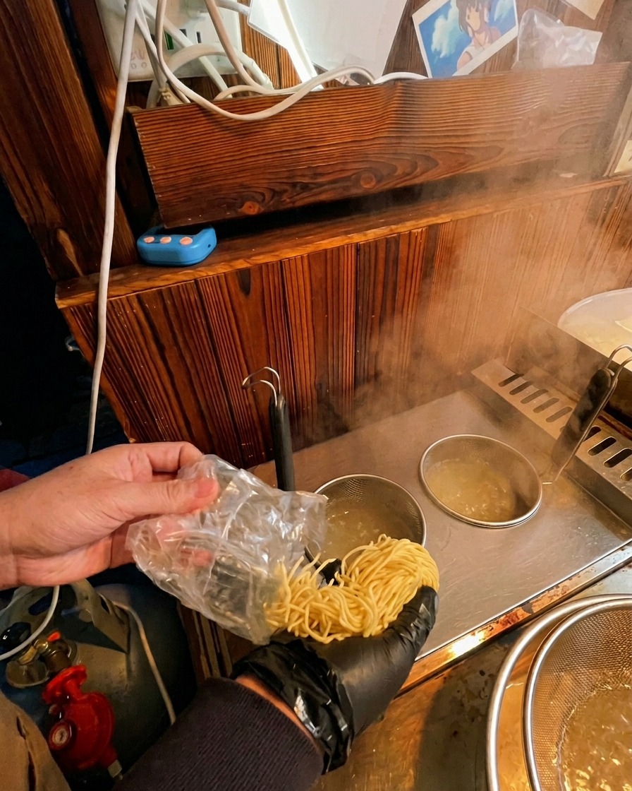 Wsypywanie świeżego makaronu ramen z opakowania do metalowego koszyka w garnku z wrzącą wodą.
