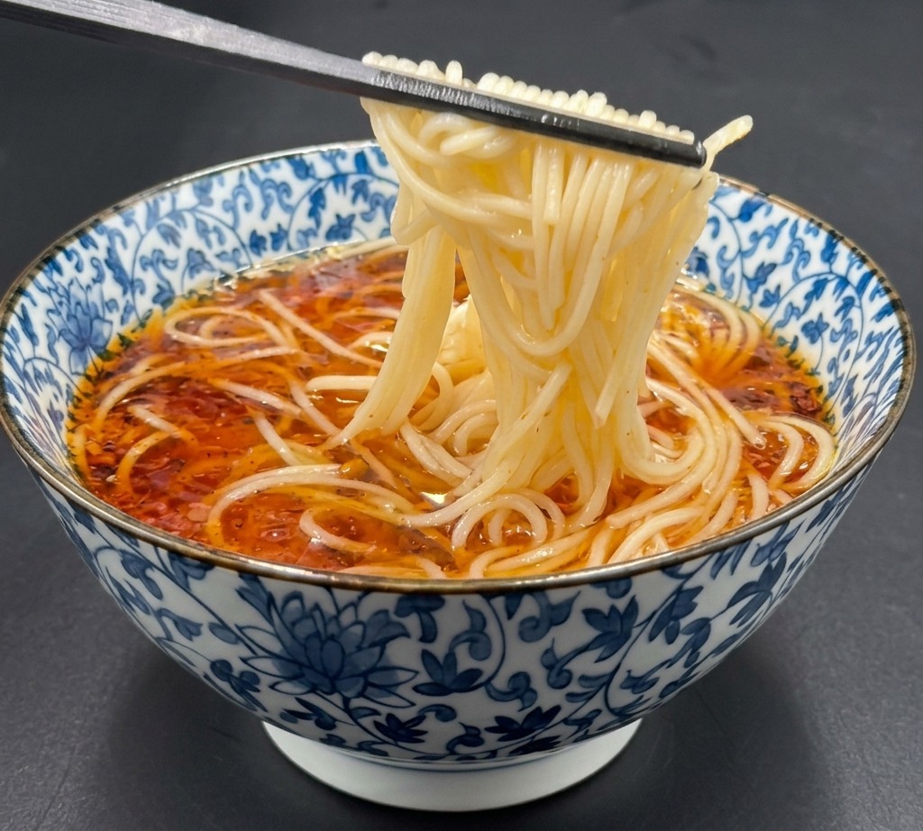 Pałeczki podnoszące ugotowany makaron ramen i wkładające go delikatnie do gorącego bulionu sojowego.