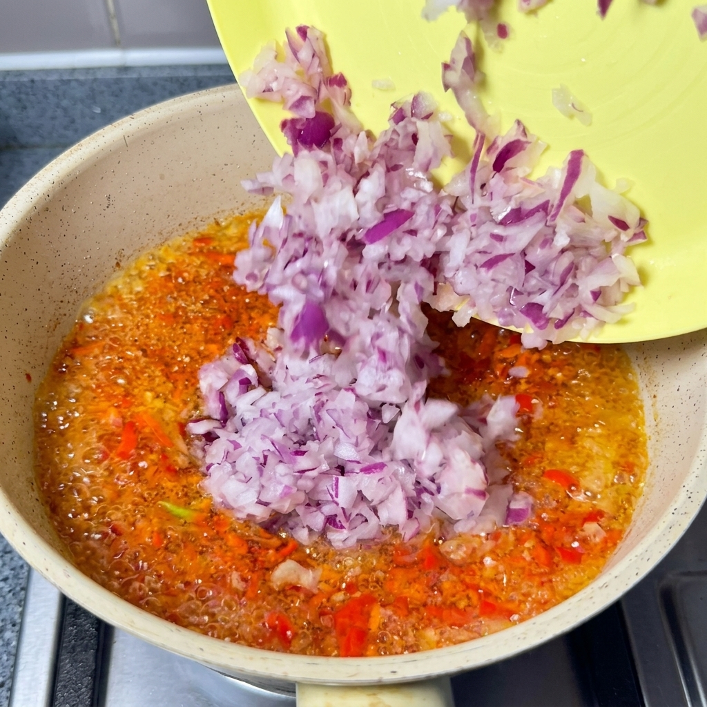 Posiekana czerwona cebula wsypywana na patelnię z gotującym się czerwonym olejem chili.