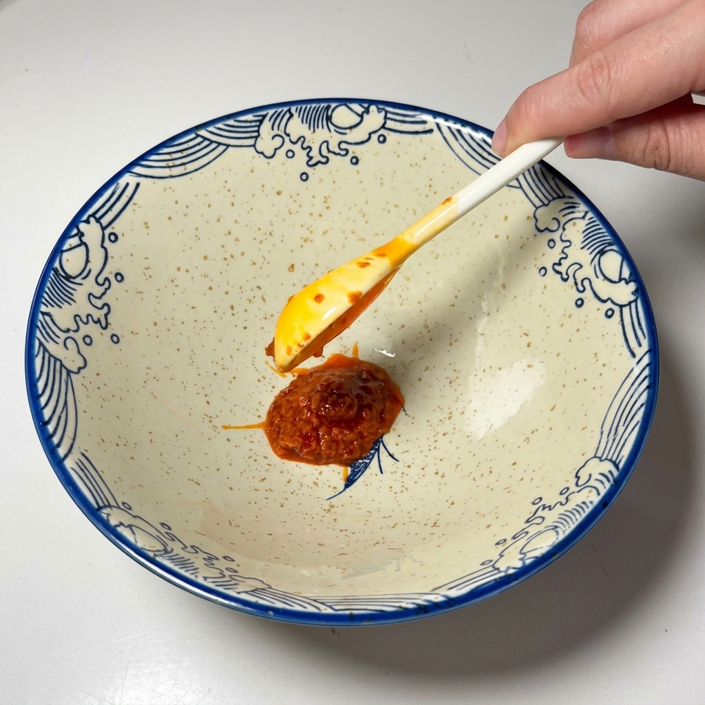 Łyżka czerwonej pasty chili nakładana na dno ceramicznej miski.