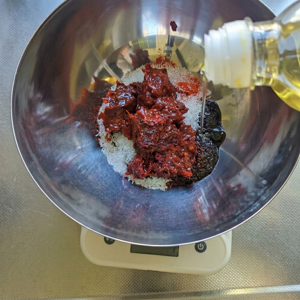 Wlewanie oleju sałatkowego do miski ze stali nierdzewnej zawierającej czerwoną pastę chili, cukier i przyprawy.