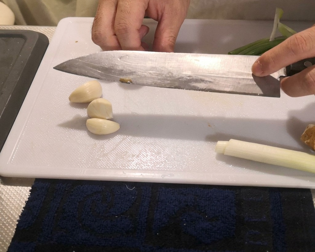 Osoba dociskająca płaską stronę noża do ząbków czosnku na desce do krojenia.