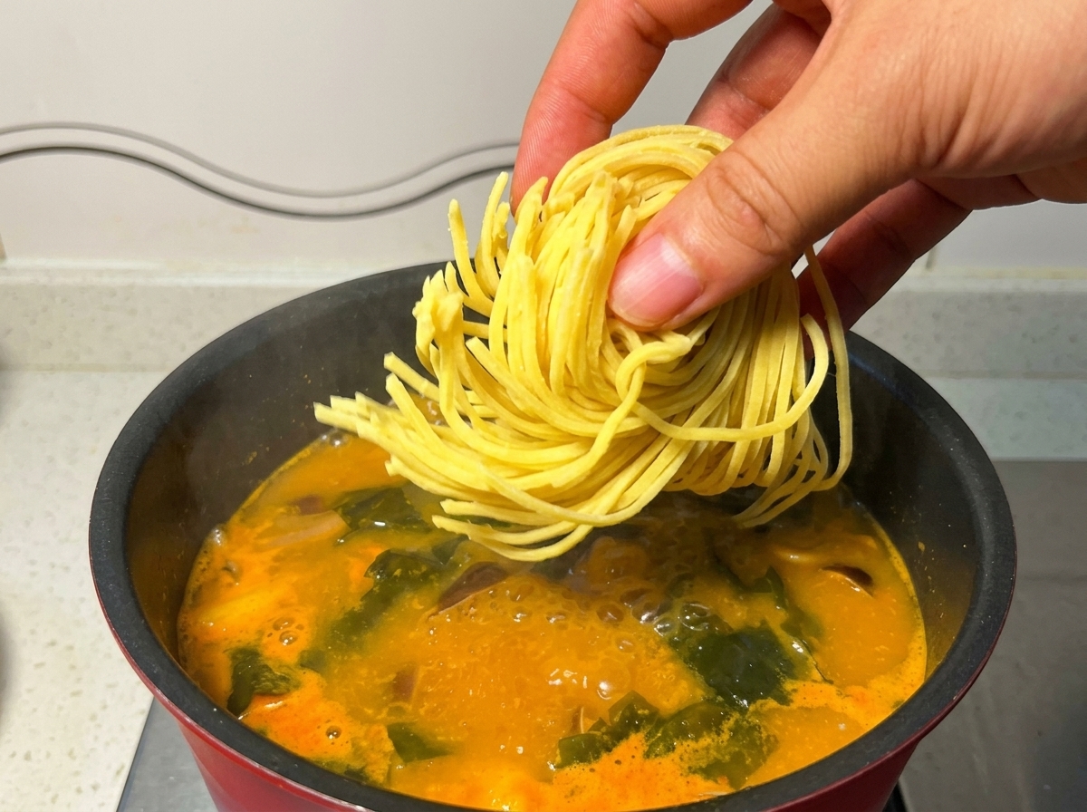 Wkładanie świeżego makaronu ramen do garnka z gorącym wywarem.