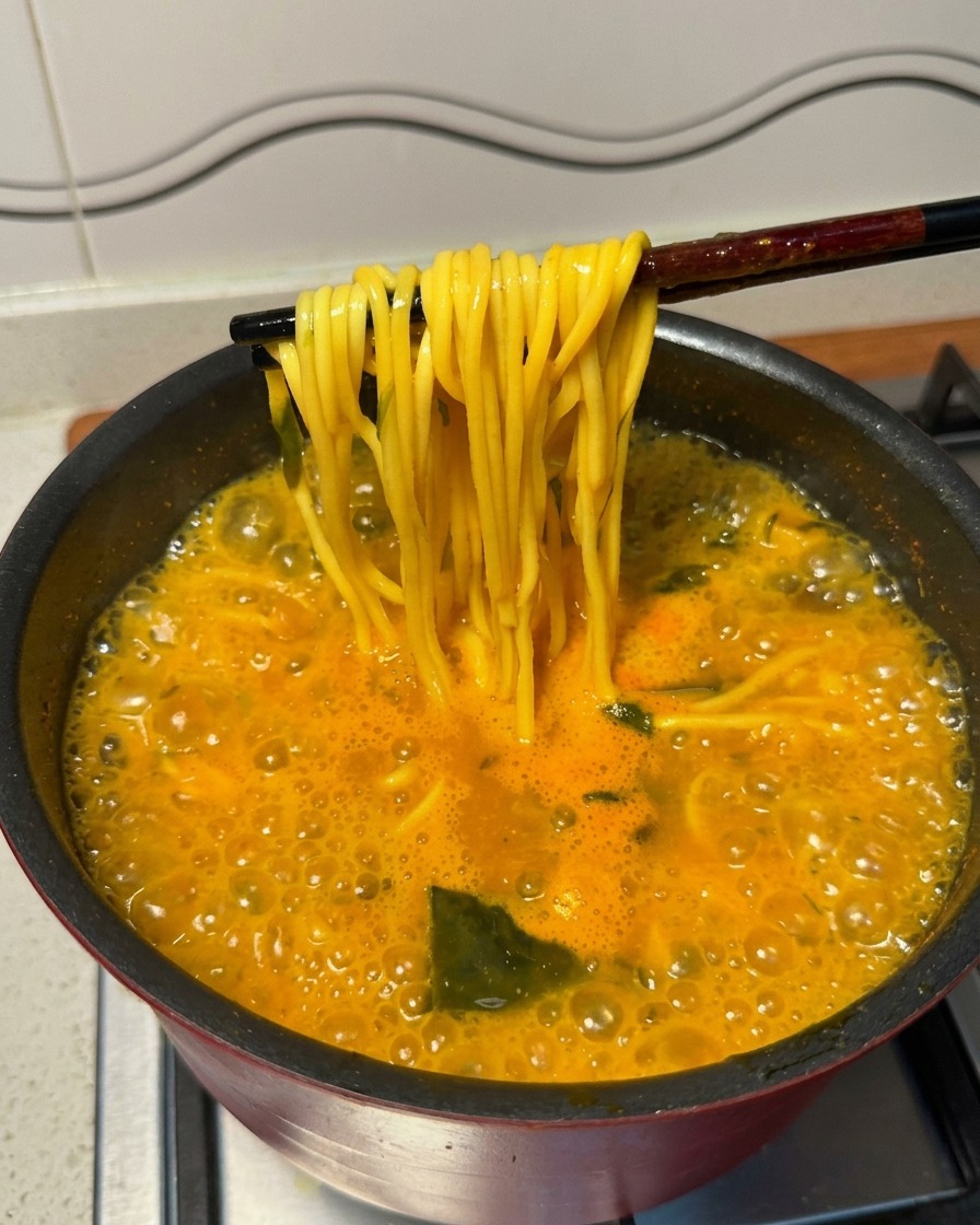 Wyciąganie żółtego makaronu ramen z zupy za pomocą czarnych pałeczek.