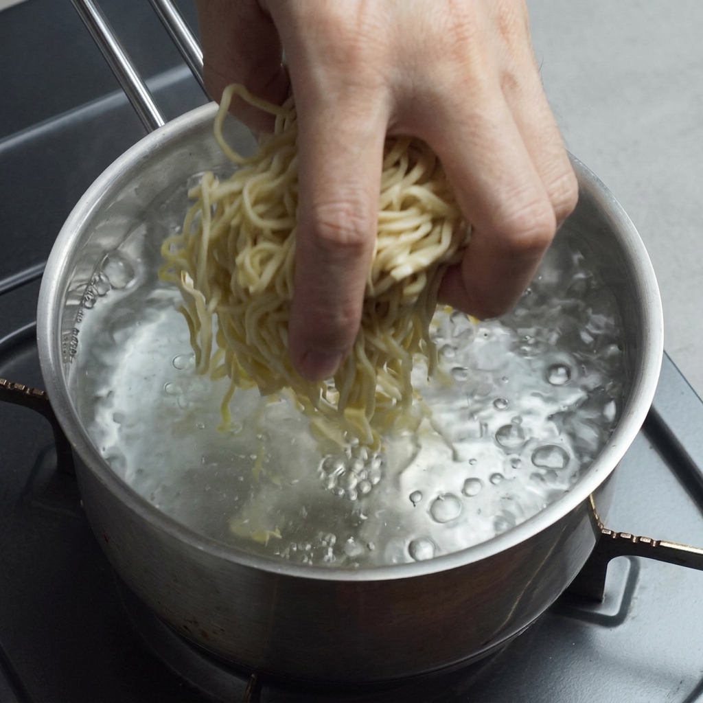 Ręka wrzucająca świeży żółty makaron ramen do garnka z mocno wrzącą wodą.