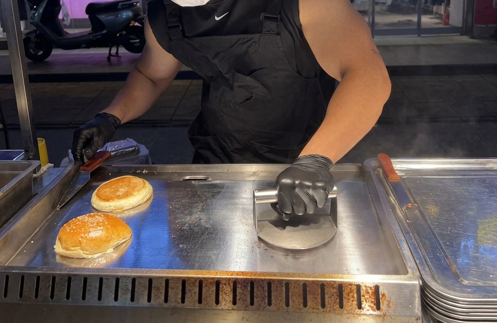 Użycie ciężkiej prasy do burgerów do mocnego spłaszczenia kulki mięsa na gorącej płycie.