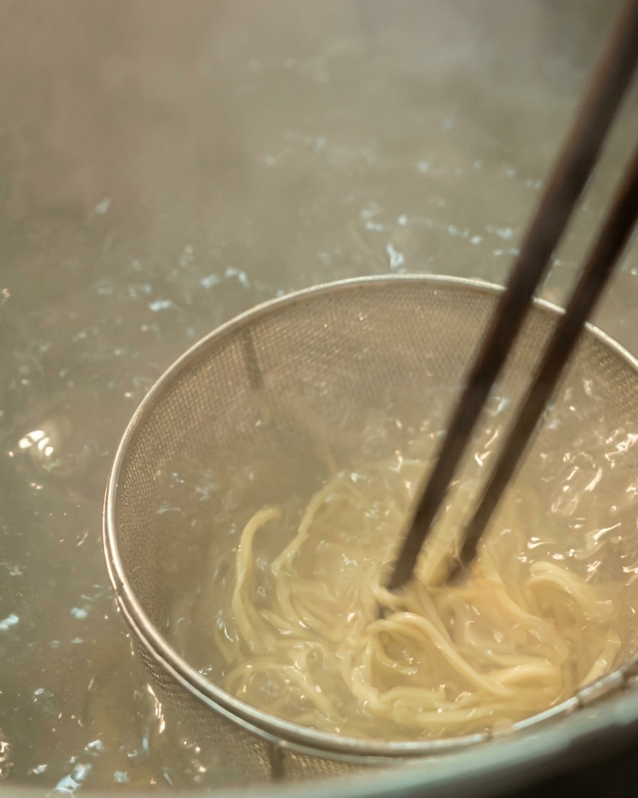 Zbliżenie na jasny makaron ramen mieszany pałeczkami we wrzącej wodzie.