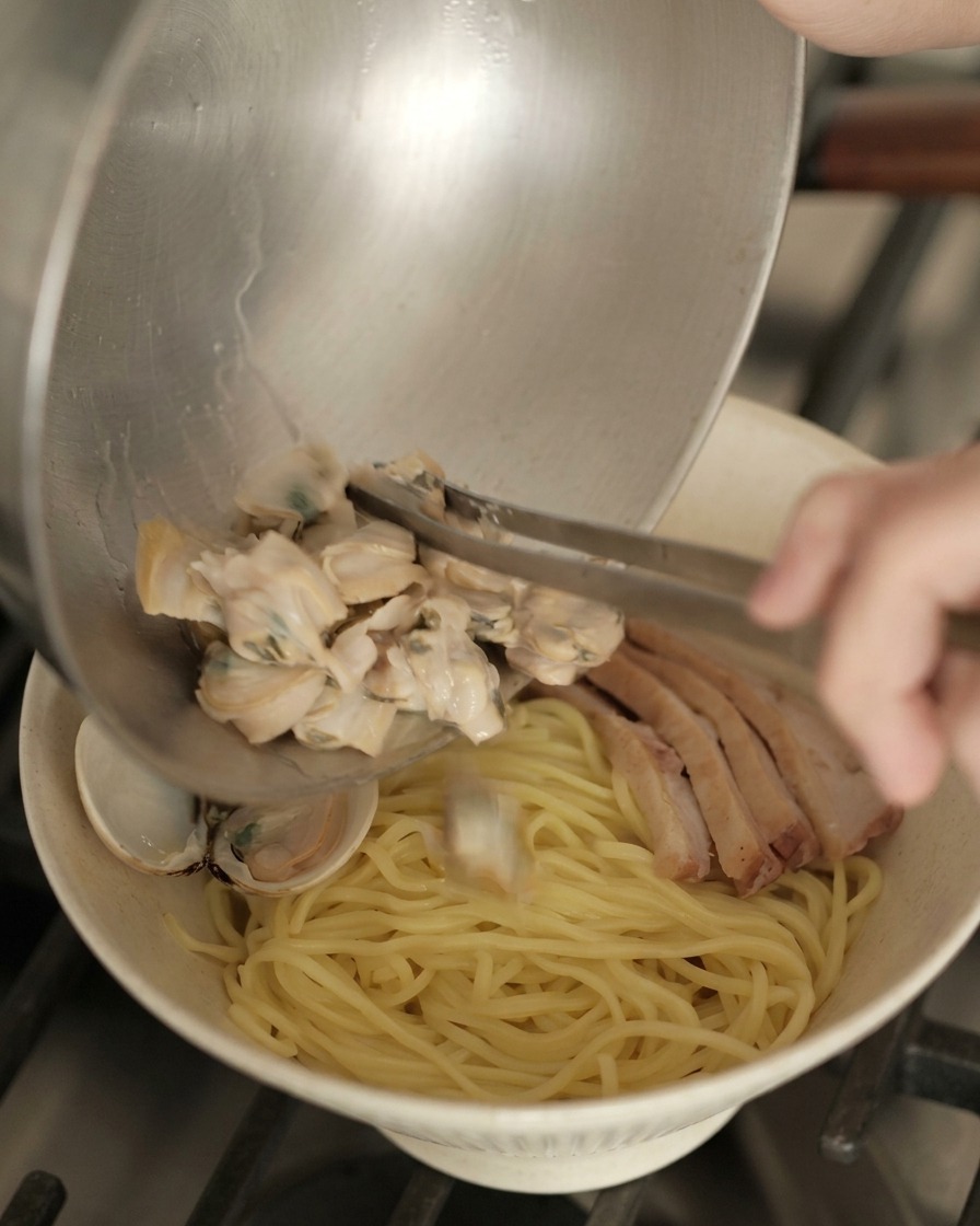 Nakładanie małży z metalowej miski na gotowy ramen z makaronem i kaczką.