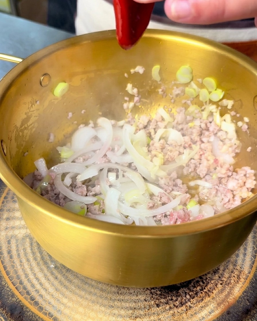 Czerwony koreański sos bibimbap wyciskany do garnka z podsmażonym mięsem i cebulą.