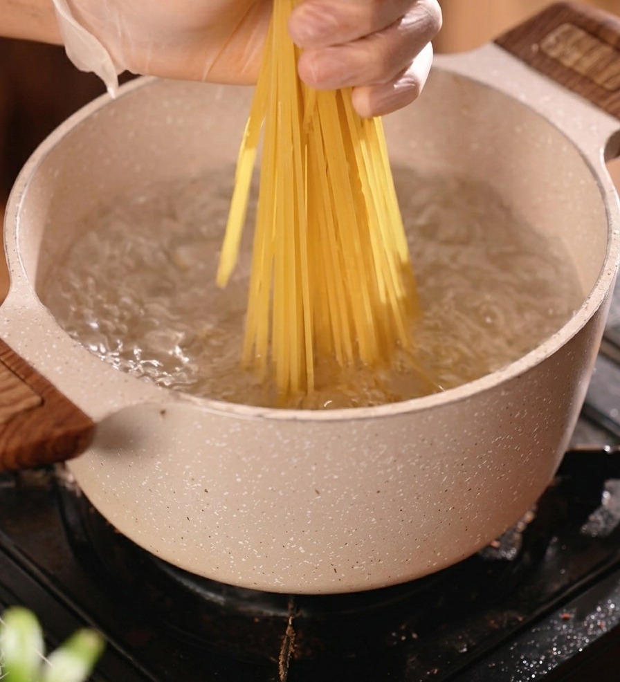 Pęczek suchego spaghetti wkładany do garnka z wrzącą wodą.