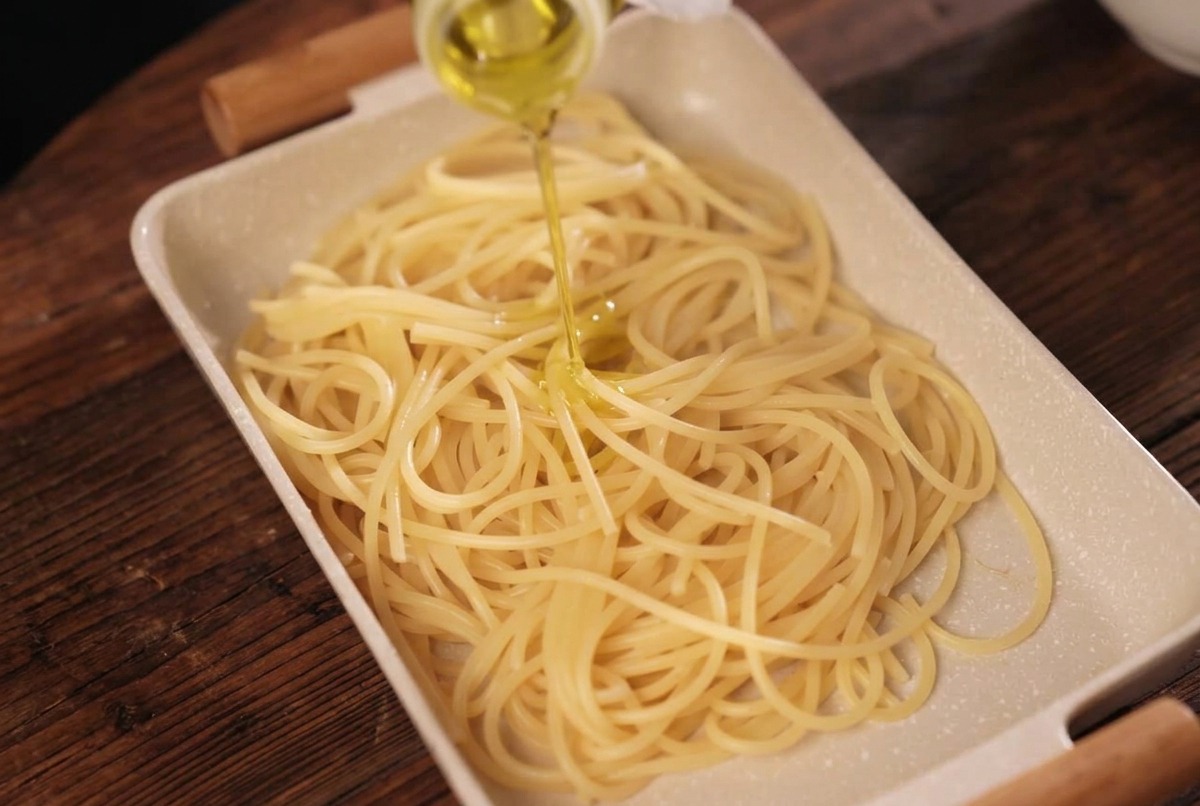 Ugotowane spaghetti na tacy, polewane złocistą oliwą z oliwek.