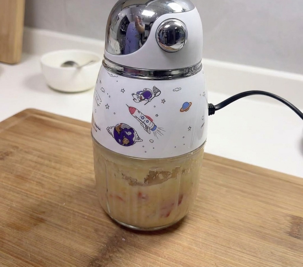 Mały blender elektryczny z motywami kosmicznymi, zawierający gęstą pastę ze zmiksowanego czosnku i czerwonych papryczek chili.