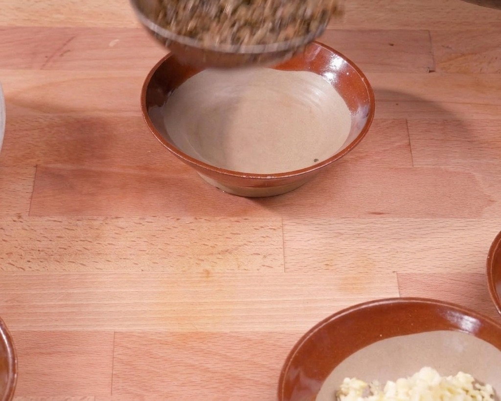 Chochla przenosząca usmażoną mieszankę wieprzowiny i warzyw do brązowej ceramicznej miski na drewnianym stole.