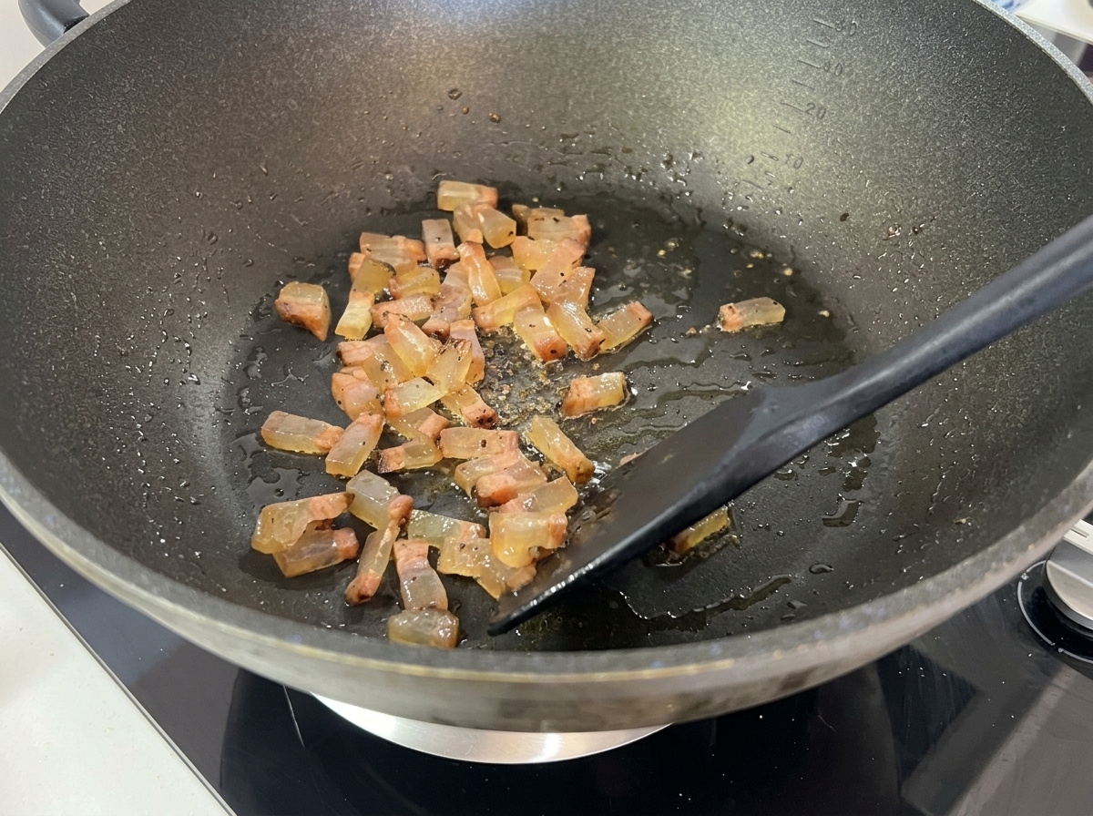 Pokrojone guanciale rumieniące się w woku i uwalniające płynny, przezroczysty tłuszcz.