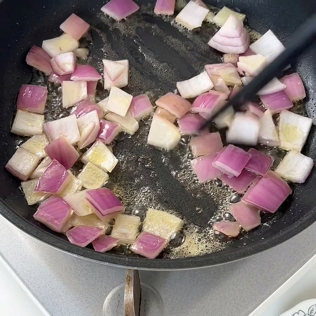 Pokrojona czerwona cebula smażąca się na maśle na nieprzywierającej patelni.