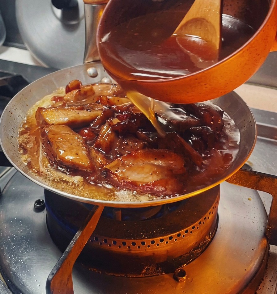 Ciemny, wyrazisty sos wlewany z małej pomarańczowej miseczki na patelnię wypełnioną kawałkami kurczaka i cebulą.