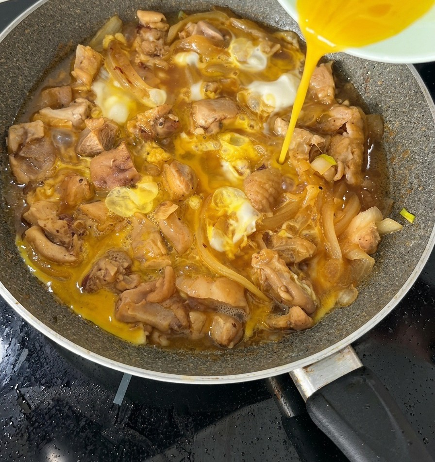Druga połowa rozkłóconych jajek wlewana na prawie gotowe danie Oyakodon na patelni.