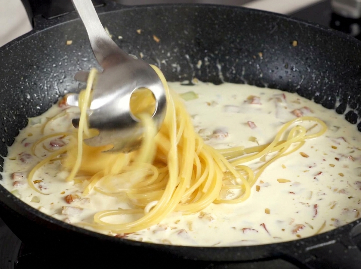 Przekładanie ugotowanego spaghetti łyżką do makaronu prosto do sosu śmietanowego.