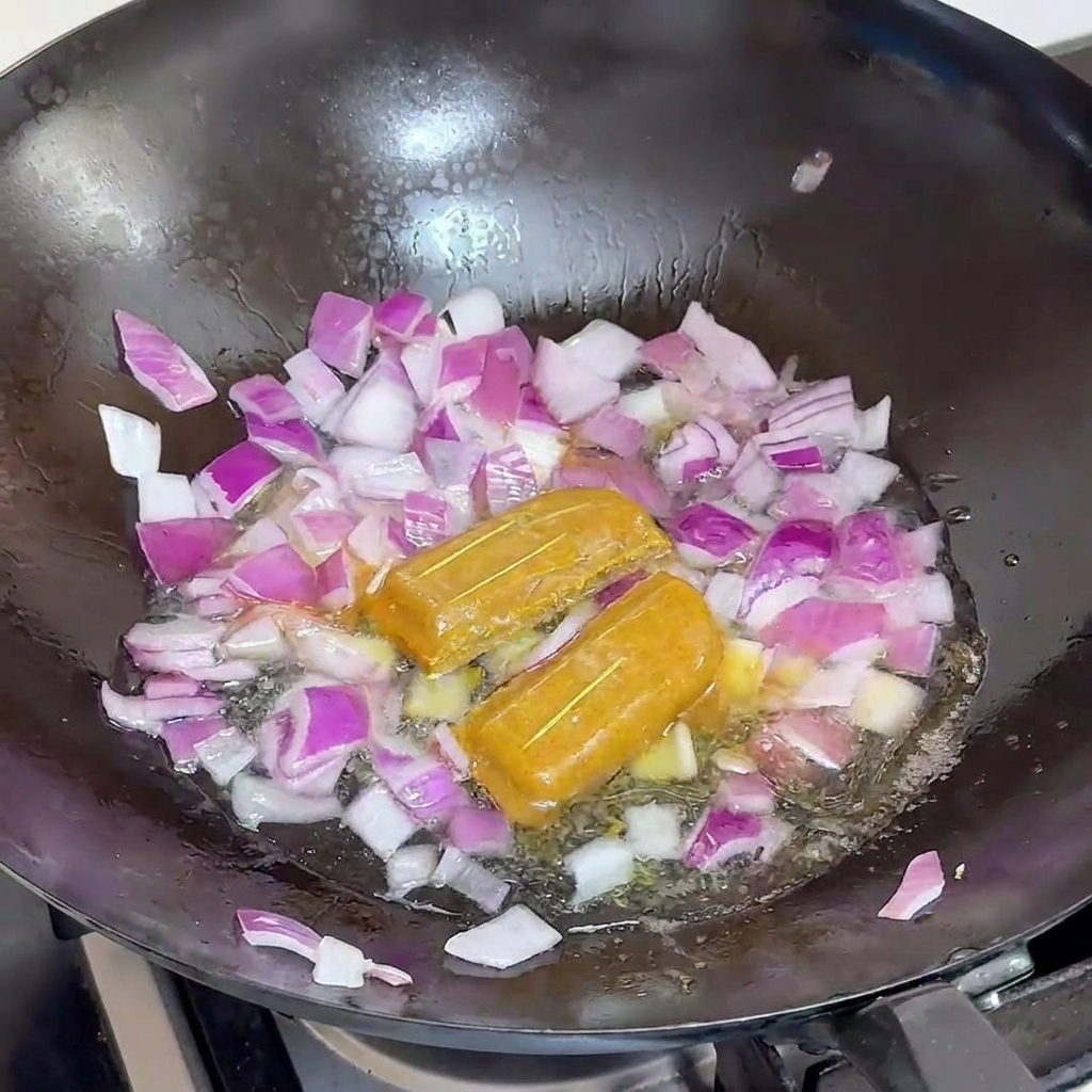 Woda wlewana do czarnego woka z czerwoną cebulą i dwiema całymi kostkami curry.