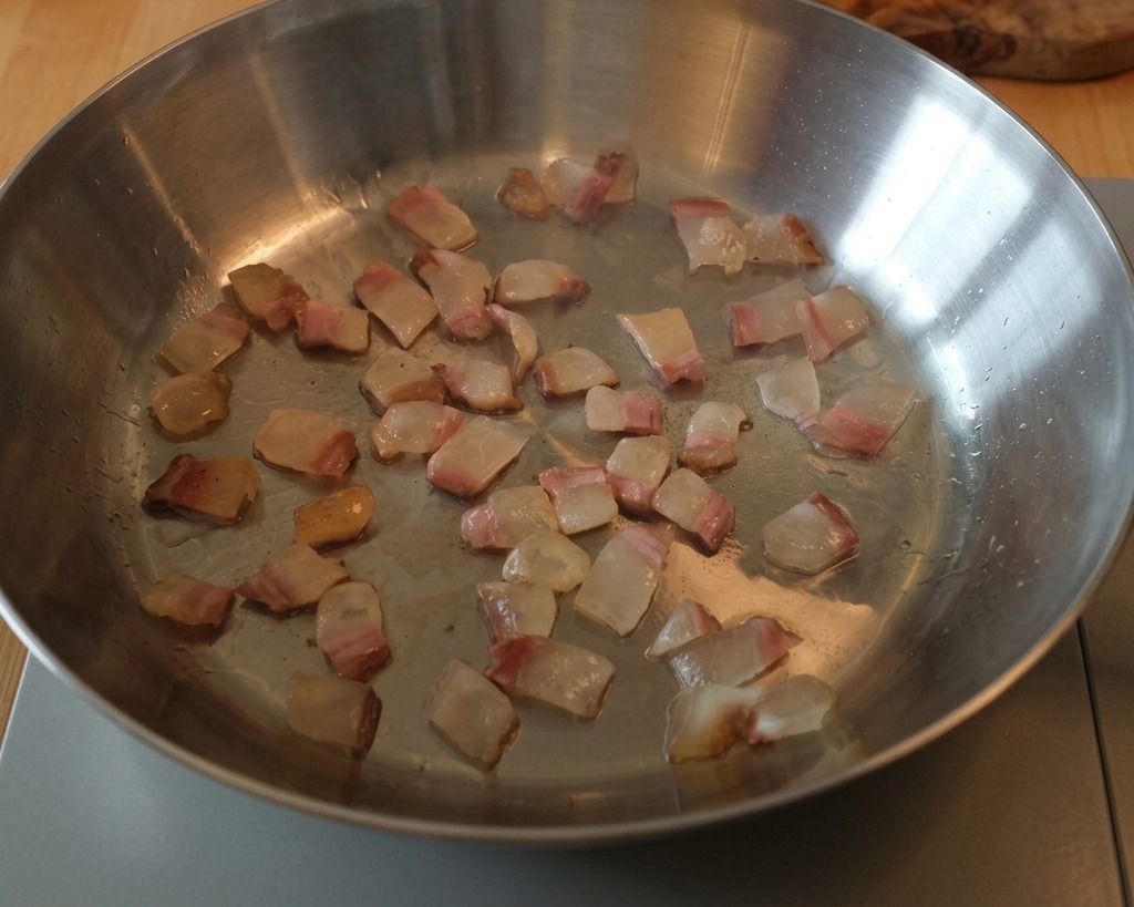 Kostki guanciale smażone na metalowej patelni, z tłuszczem zamieniającym się w klarowny płyn wokół mięsa.