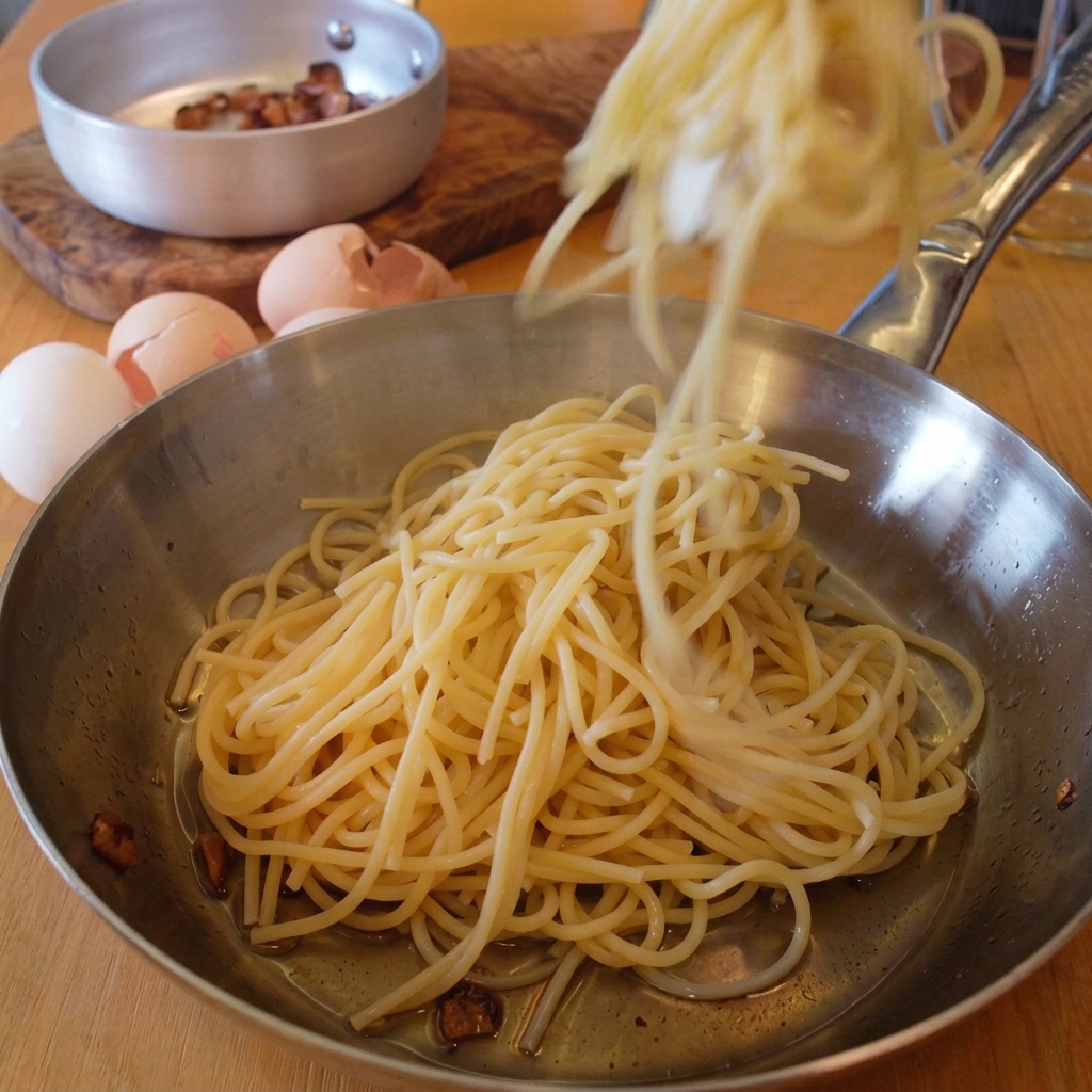 Szczypce przekładające świeżo ugotowane spaghetti na patelnię z resztkami tłuszczu z guanciale.
