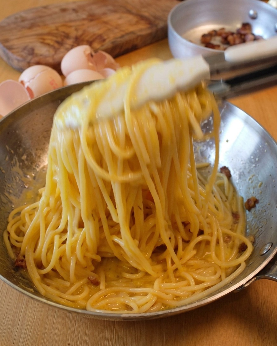 Energiczne mieszanie spaghetti na patelni za pomocą szczypiec w celu uzyskania kremowego sosu.