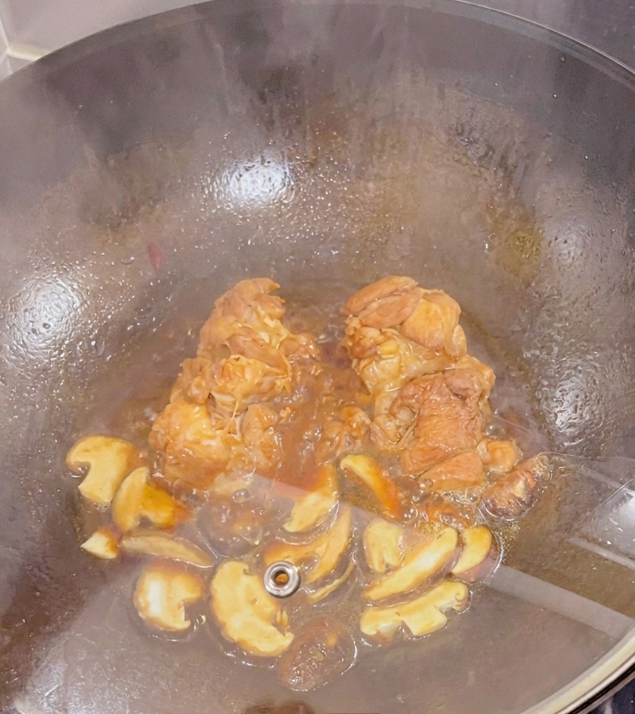 Udka z kurczaka i pokrojone grzyby shiitake duszące się w ciemnym sosie pod szklaną pokrywką w woku.