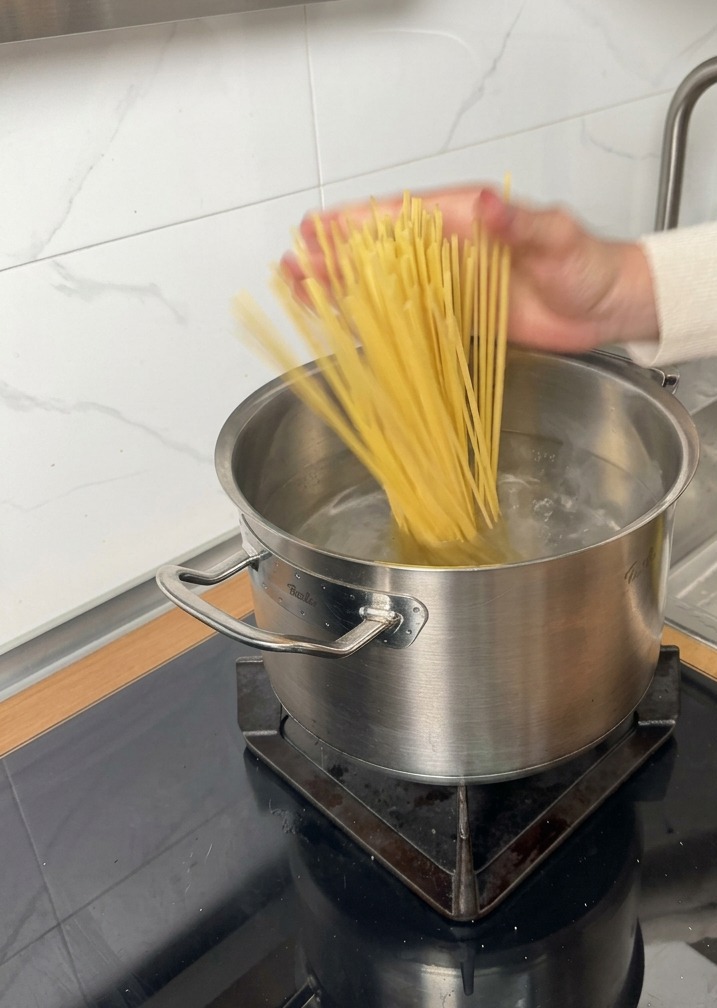 Makaron linguine wkładany do garnka z wrzącą wodą na płycie indukcyjnej.